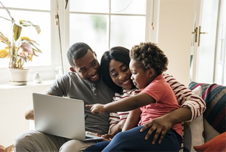 Familia sonriendo mientras niña apunta a pantalla de notebook